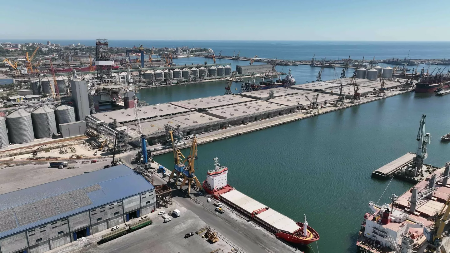 Building data - Aerial view of a busy industrial port with cargo ships, cranes, warehouses, and large grain silos along the waterfront.